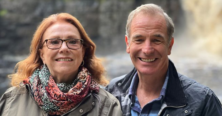 Robson Green and Melanie Hill smiling at camera with High Force Waterfall in the background © BBC